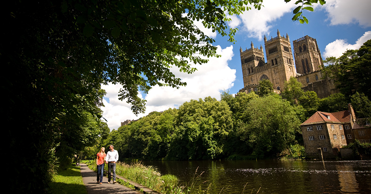 couple walking along river bank in Durham City with Durham Cathedral in background